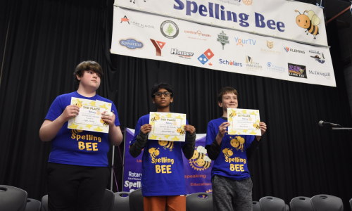 Three students hold certificates after participating in a Spelling Bee.